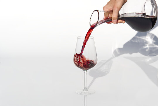 Sommelier pours red wine from decanter to wineglass on white background.