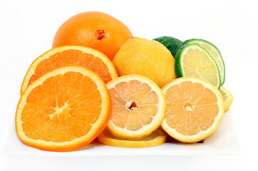 Citrus fruits of oranges, lemons and limes cut and whole on a white plate and background.