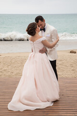 Fototapeta na wymiar Latino Bride and groom with white tuxedo holding each other at the beach