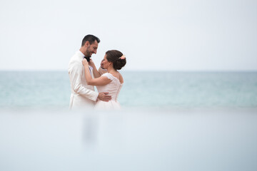 Latino Bride fixing grooms bow tie at the beach with blurred reflection