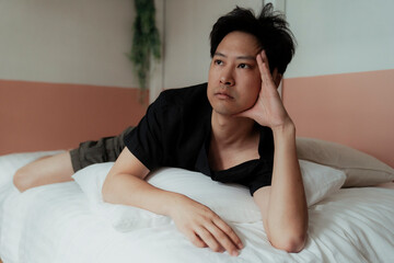 Gay in black t-shirt lie down on the white bed with a pillow under his chest.