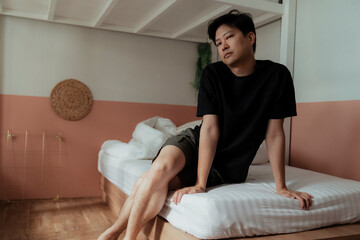 Asian gay in t-shirt sitting on the white bed with sexy posture and eyesight.