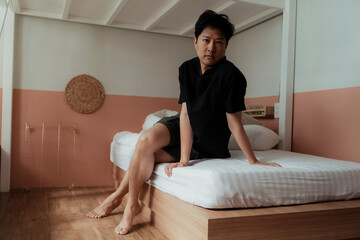 Gay sit on the bed with crossed leg.