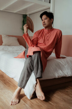 Gay in orange collar sitting with gorgeous posture on the white bed white chinese folding fan.