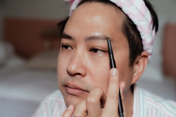 Gay with pink headband draw his eyebrow in the bedroom.