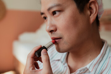 Gay makeup his lip with red lipstick in the bedroom.