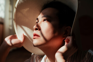Gay chin up and face to the sun while he sitting at the window with white hat.