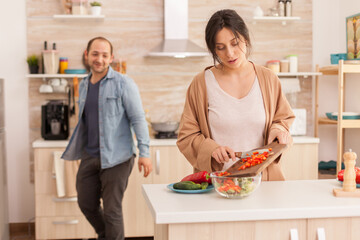 Wife making healthysalad in kitchen from fresh vegetables. Happy in love cheerful and carefree couple helping each other to prepare meal