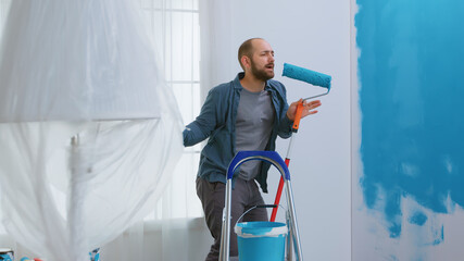 Repairman singing on roller brush dipped in blue paint while redecorating apartment. Housework,...
