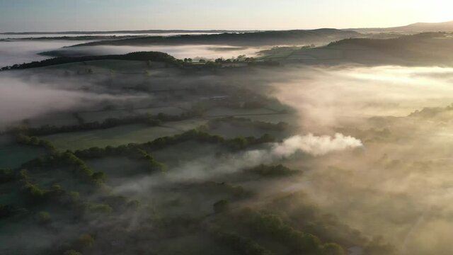 Aerial clip of rolling Devon countryside in dawn mist, Brentor, Devon, England