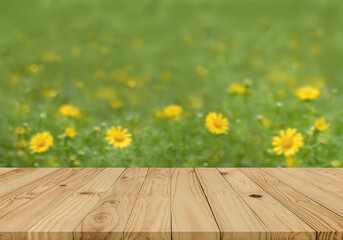 Empty brown plank wooden board mock up display as shelf or desk with blurred background group of yellow flowers in the green field.