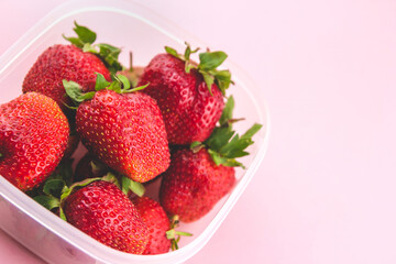 Ripe garden strawberries in a transparent container on a pink background copy space. Strawberry harvest.