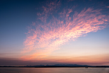 The clouds reflect the colorful sunset over Puget Sound as the sun slowly sets behind the mountains