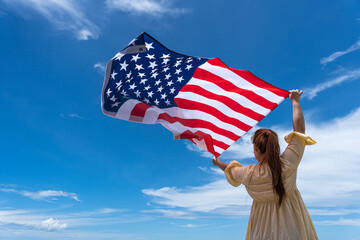 woman standing and holding USA flag under blue sky.