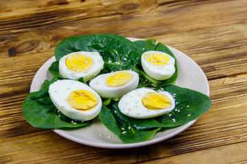 Boiled eggs with fresh spinach leaves and sesame seeds on wooden table