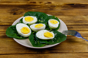 Boiled eggs with fresh spinach leaves and sesame seeds on wooden table