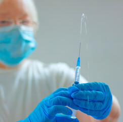 vaccination, covid vaccination or treatment of the disease. Close-up of a doctor's gloved and masked hand holding a medical syringe on a gray background.