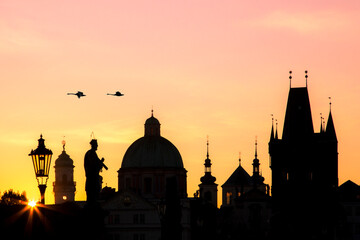 Obraz premium Prague cityscape at sunrise showing silhouettes of buildings, lanterns, statues against the colourful sky and a couple of flying swans 