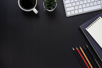 Top view above of Black office desk table with keyboard, notebook and coffee cup with equipment...