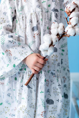 Little girl in a white dress holds a sprig of cotton in her hands