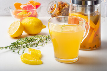 Sweet fruit and herbal tea in a transparent Cup on a light background with marmalade and a teapot.