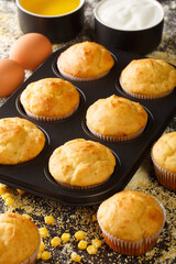 Freshly baked corn muffins in a baking dish and ingredients close-up on the table. vertical