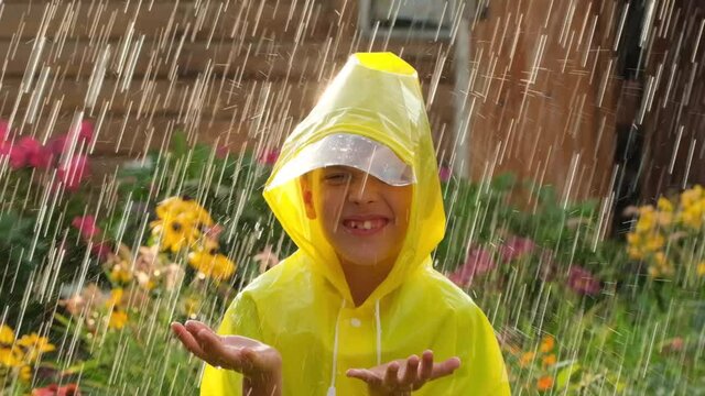 Little happy cheerful boy child wearing yellow raincoat and enjoying having fun rainfall. Kid playing with drops rain in sunlight, Happy family summer autumn fall childhood dream concept 120 slow-mo