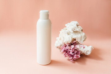 Blank white bottle on pink background, white stone and pink dried flower as decor. Natural organic cosmetics, sustainable lifestyle concept. Front view, copy space.