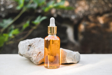 Bottles of orange serum next to natural stones against a gray wall with grape leaves with natural light. Trendy style. Grape extract. Cosmetic mockup. Copyspace.