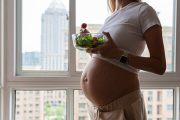 Happy young pregnant woman eating vegetable salad at home. Healthy nutrition and pregnancy concept....