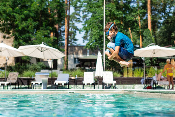 side view of boy in t-shirt and swim goggles plugging nose while jumping into pool
