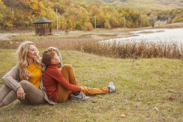 Happy family resting in the park at warm autumn weather.  Woman and boy wearing fal style clothes. Two pwople are happy spending time together