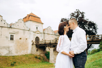 Stylish young man in white shirt and woman in luxury long dress on wedding day near the castle.