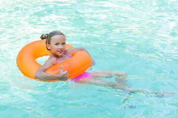 pleased girl floating in pool on inflatable ring and showing thumb up