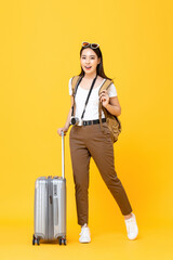 Full length portrait of smiling cute young Asian woman tourist with luggage isolated on yellow studio background