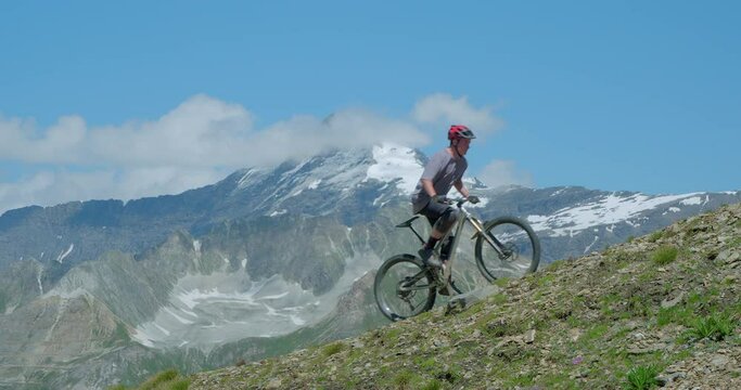 Two mountain bikers peddling hard up a steep high altitude mountainside with glaciers in background.  Peddling up steep mountains at 12,000ft above sea level is extremely demanding on the human body.