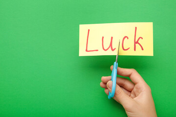Cut paper with word LUCK and scissors on green background, closeup. Hand holding card with the text luck.