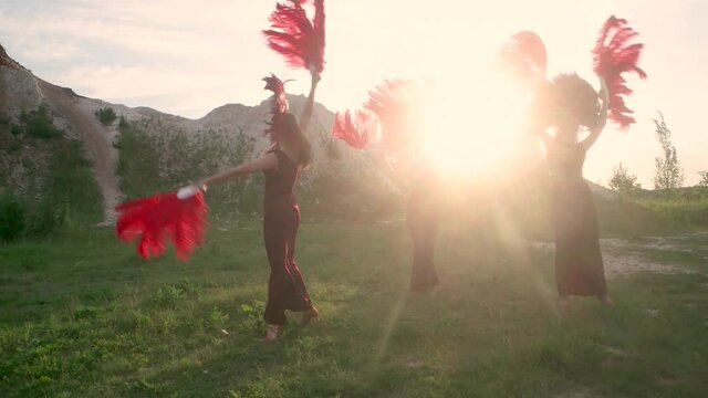 women in red carnival costumes dance in the sunlights in nature. Slow motion