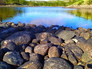 Naklejka na ściany i meble Large black stones on the lake shore