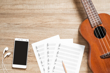Top view of ukulele with blank stave pad bar for music notes and smartphone on wood texture background