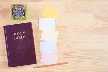 Top view of Holy Bible and paper notes on wooden background
