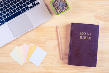 Top view of Holy Bible, paper notes, laptop, and succulent plant on wooden background
