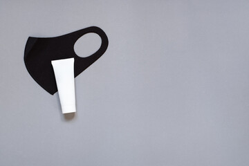 Top view of black protective mask and white tube on grey background with copy space