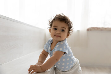 Portrait of adorable little african american baby boy or girl relying on furniture, learning making...