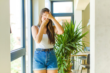 young pretty woman covering face with both hands saying no to the camera! refusing pictures or...