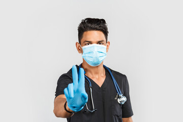  Indian / Asian doctor with stethoscope wearing blue medical face mask and gloves on gray background. protection against coronavirus