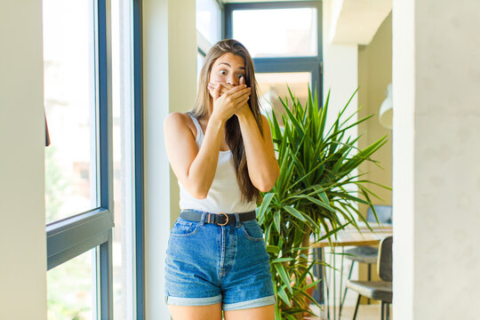 young pretty woman covering mouth with hands with a shocked, surprised expression, keeping a secret or saying oops