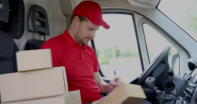 delivery service man sitting in van and writing documents on clipboard before delivering a package to customer