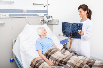 Experienced doctor holding X-ray of spine of an elderly woman. Patient and the doctor are smiling because the woman's spine health is fine. Treatment of spine disease, osteochondrosis