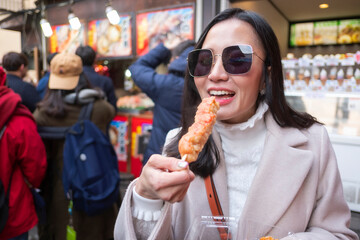 Young tourist woman eating yakitori, chicken grilled as the famous street food at bamboo forest Arashiyama in Japan